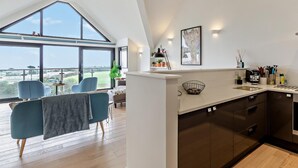 A modern kitchen with a large window, a dining area with chairs, and a view of the landscape. - 2 Bed in Helston (oc-45739) (Kuggar)