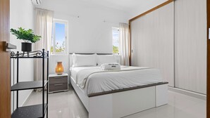 A bedroom with a bed, a nightstand, a potted plant, a lamp, and a wardrobe. - Modern 3BR Villa With Private Pool in Oasis del Lago by Vistacana Rentals (Punta Cana)