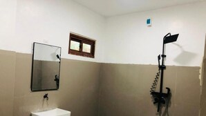 A small bathroom with a sink, mirror, shower, and a window.