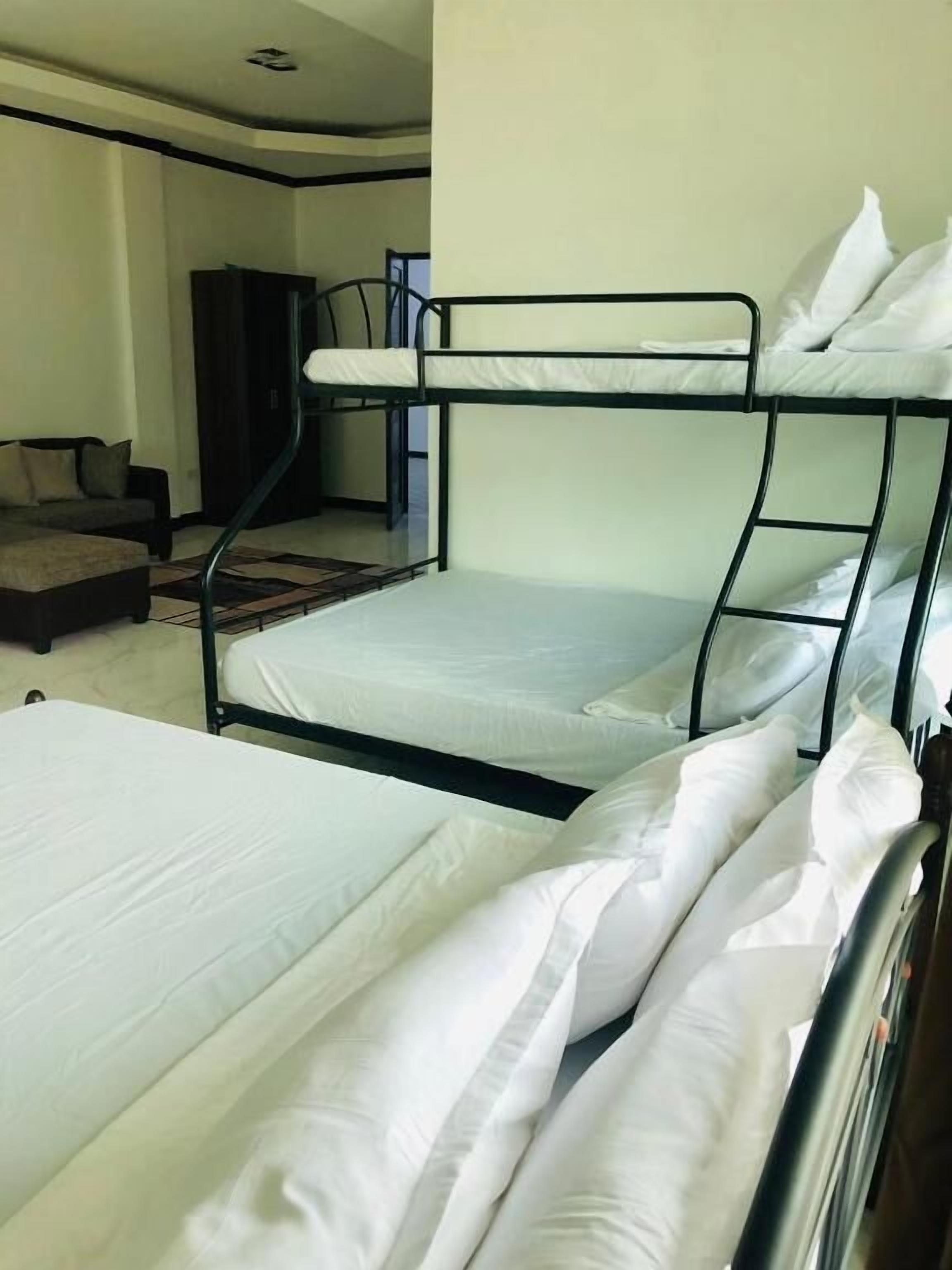 A bunk bed with white bedding, a sofa, and a staircase in a room with plain walls.