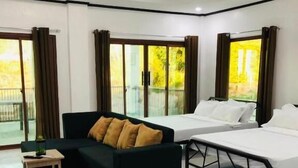 A modern hotel room with a bed, a sofa, a small table, and a view of the outdoors.