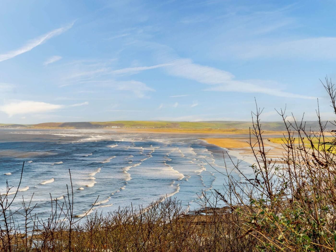 A coastal landscape with a view of the sea, distant hills, and sparse vegetation.