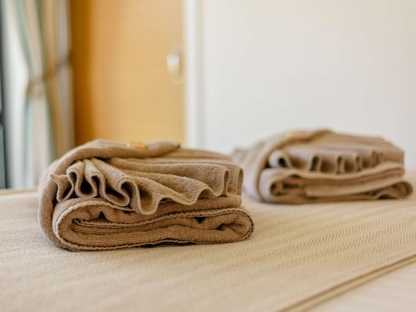 Ein ordentlich gefaltetes, beige Handtuch auf einer strukturierten Oberfläche, vermutlich einem Bett oder Handtuchhalter.