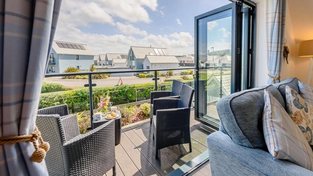 A balcony with wicker furniture, a sofa, and a view of modern buildings. - 3 Bed in Bideford (oc-46252) (Northam)