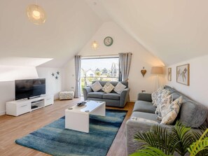 A modern living room with a flat-screen TV, a sofa, a coffee table, and a large window with curtains. - 3 Bed in Bideford (oc-46252) (Northam)