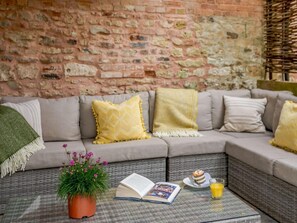 Eine gemütliche Sitzecke mit Backsteinwand, einer Couch mit Kissen, einem kleinen Tisch mit einem Buch, einer Topfpflanze und einem Glas Orangensaft.