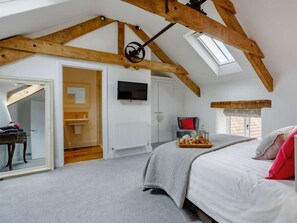Ein Schlafzimmer mit schrägem Dach, einem Bett, einem Fernseher und einem Fenster.