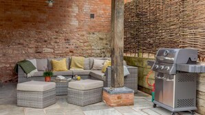 A cozy outdoor seating area with a sectional sofa, ottomans, and a grill. - 4 Bed in Honiton (oc-45563) (Payhembury)