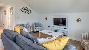 En moderne stue med sofa, lænestole, fjernsyn og dekorativ vægkunst.
