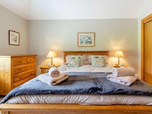 Ein ordentlich bezogenes Bett mit blauer Decke, zwei Nachttischlampen und einem hölzernen Kopfteil.