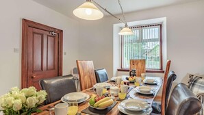 Een eetkamer met een houten tafel gedekt voor het ontbijt, inclusief borden, bekers en een fruitmand.