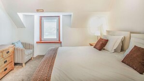Een slaapkamer met een bed, een stoel, een kaptafel, een raam en een plafondlamp.