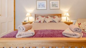 Ein ordentlich bezogenes Bett mit floralen Kissen, zwei Nachttischlampen und ein Paar Handtücher auf dem Bett.