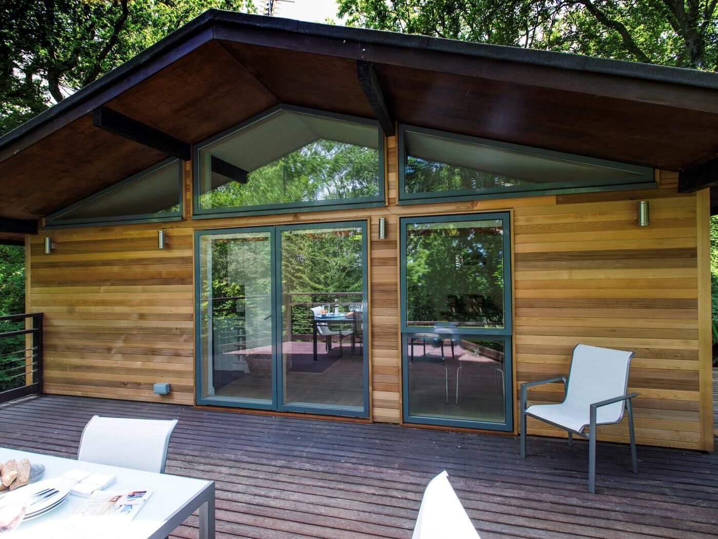 Une cabane moderne en bois, dotée de grandes portes-fenêtres coulissantes, d’une terrasse avec coin salon extérieur et d’un patio couvert.
