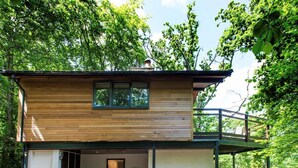 A two-story wooden cabin with a balcony, a covered porch, and a small entryway. - 2 Bed in Beaulieu (oc-nfl71) (Beaulieu)