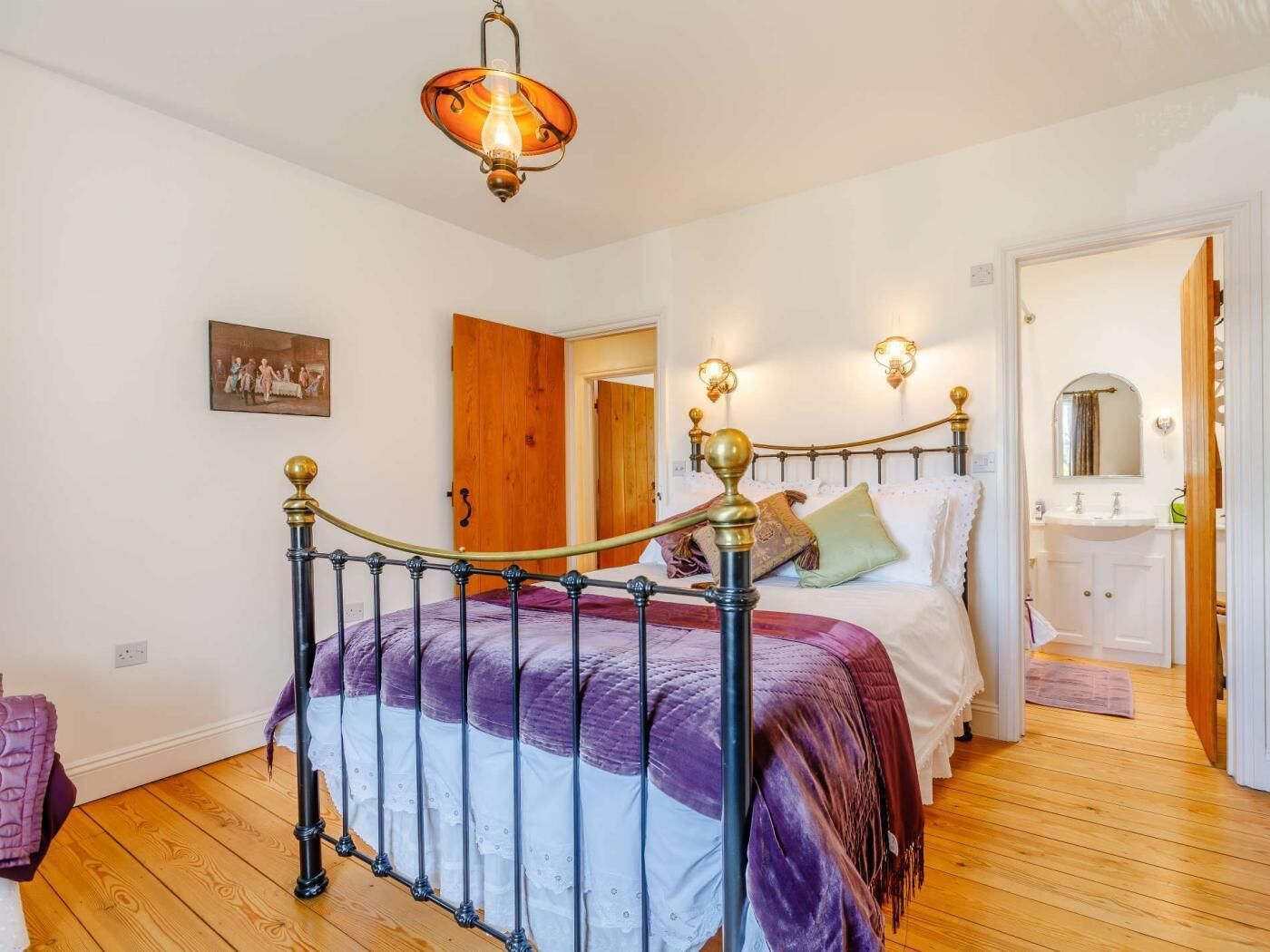 A bedroom with a bed, a wooden door, a white wall, and a light fixture.