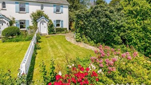 A two-story house with a white exterior and blue shutters, surrounded by a well-maintained garden with various plants and flowers. - 2 Bed in Sway (oc-nfl43) (Sway)