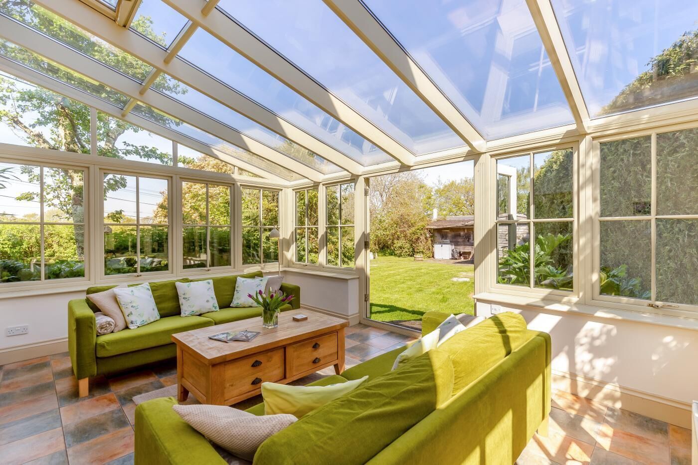 Una veranda con un divano verde, un tavolino in legno e vista su un giardino.