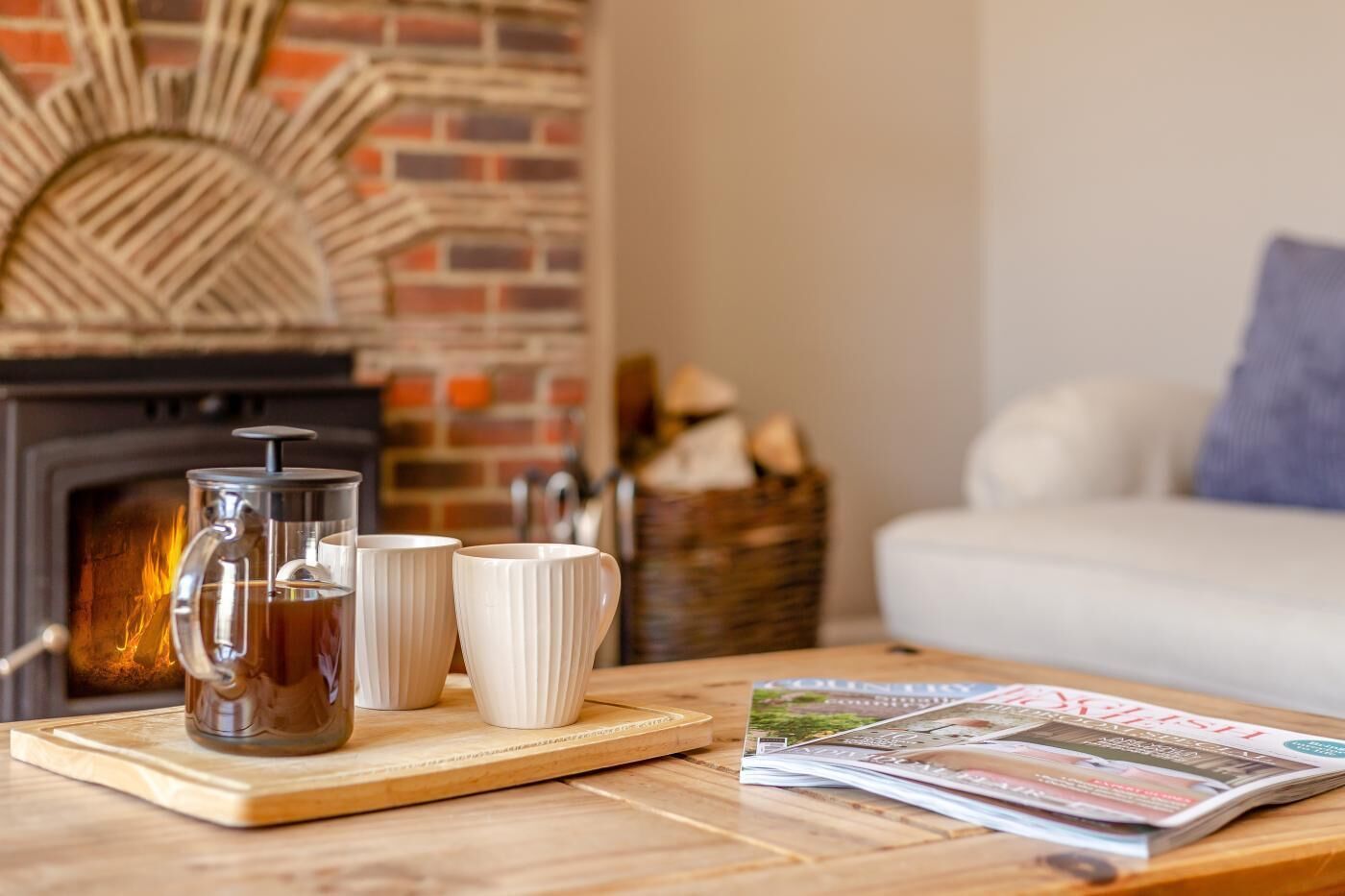 A wooden table with a coffee pot, two white mugs, and a magazine.