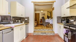 A compact kitchen with white cabinets, a dishwasher, a stove, and a dining area with a table and chairs. - 2 Bed in Aberaeron (oc-45333) (Aberaeron)