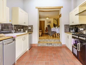 A compact kitchen with white cabinets, a dishwasher, a stove, and a dining area with a table and chairs. - 2 Bed in Aberaeron (oc-45333) (Aberaeron)