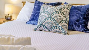 A neatly made bed with a striped white duvet, two pillows with geometric patterns, and a bedside lamp on a wooden nightstand. - 2 Bed in Aberaeron (oc-45333) (Aberaeron)