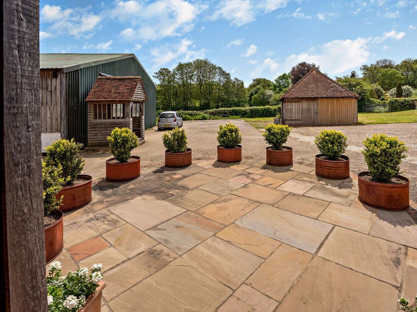 A courtyard with stone paving, wooden buildings, and potted plants.
