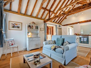 Ein gemütliches Wohnzimmer mit einem blauen Sofa, Holzbalken, einem weißen Schrank und einer Küchenzeile.