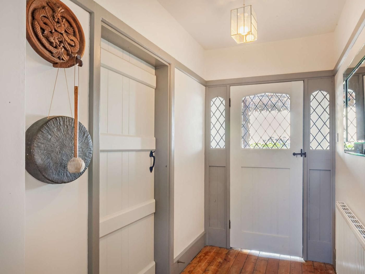 A hallway with a wooden floor, a white door with a window, and a wall-mounted decorative object.