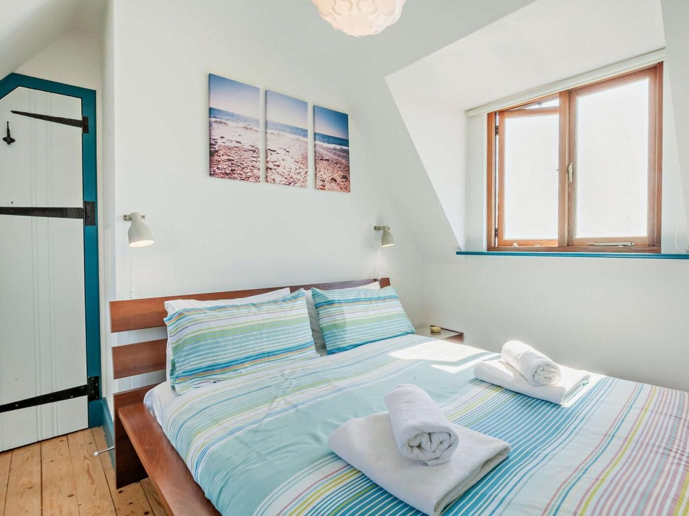 A bedroom with a bed, pillows, a window, and a wall-mounted picture.