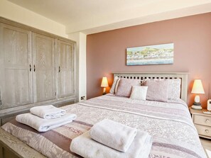 A bedroom with a bed, two bedside lamps, a painting on the wall, and a wardrobe. - 2 Bed in Pevensey (oc-bt070) (Pevensey Bay)