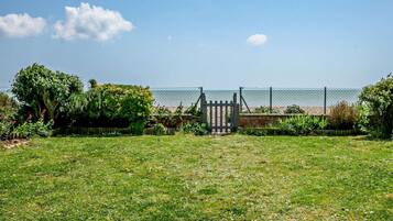 A grassy area with a gate leading to a beach, surrounded by greenery and a fence.