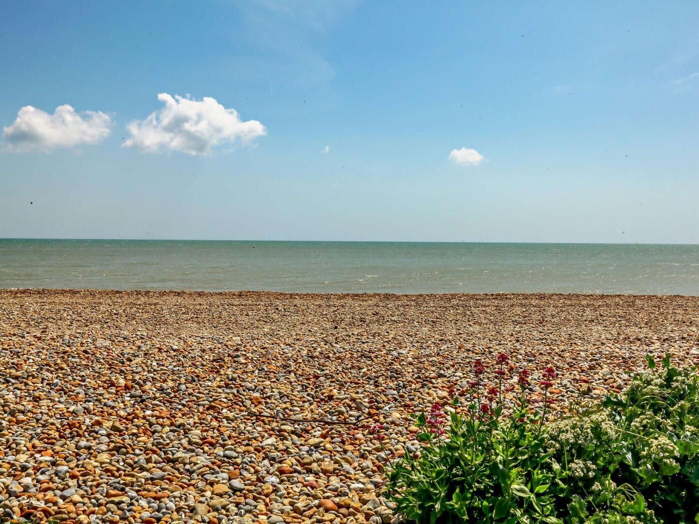 A pebbled beach with a clear sky and calm sea.