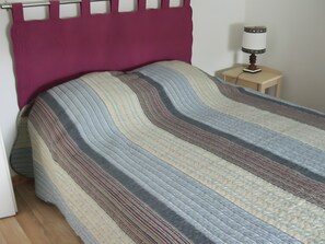 A bed with a striped bedspread, a wooden nightstand with a lamp, and a door to the left.
