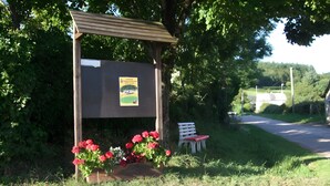A wooden shelter with a bench and flowers, surrounded by greenery. - Le gîte du "Grand Reu" - Gîte Anna (Corancy)