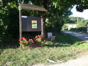 A wooden shelter with a bench and flowers, surrounded by greenery. - Le gîte du "Grand Reu" - Gîte Anna (Corancy)