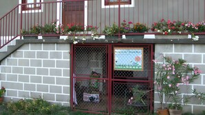 A two-story building with a balcony, a window with a metal grill, and a sign on the ground floor. - Le gîte du "Grand Reu" - Gîte Anna (Corancy)
