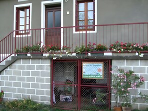 A two-story building with a balcony, a window with a metal grill, and a sign on the ground floor. - Le gîte du "Grand Reu" - Gîte Anna (Corancy)