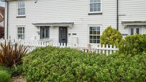 A two-story white building with a white picket fence, numbered doors, and a small garden area with bushes. - 2 Bed in Camber (oc-bt084) (Camber)