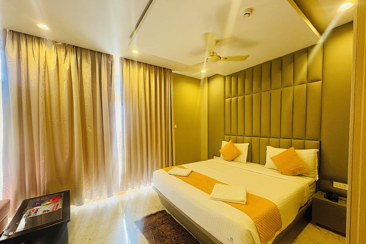 Una habitación de hotel con cama, mesita de noche, ventilador de techo y ventana con cortinas.