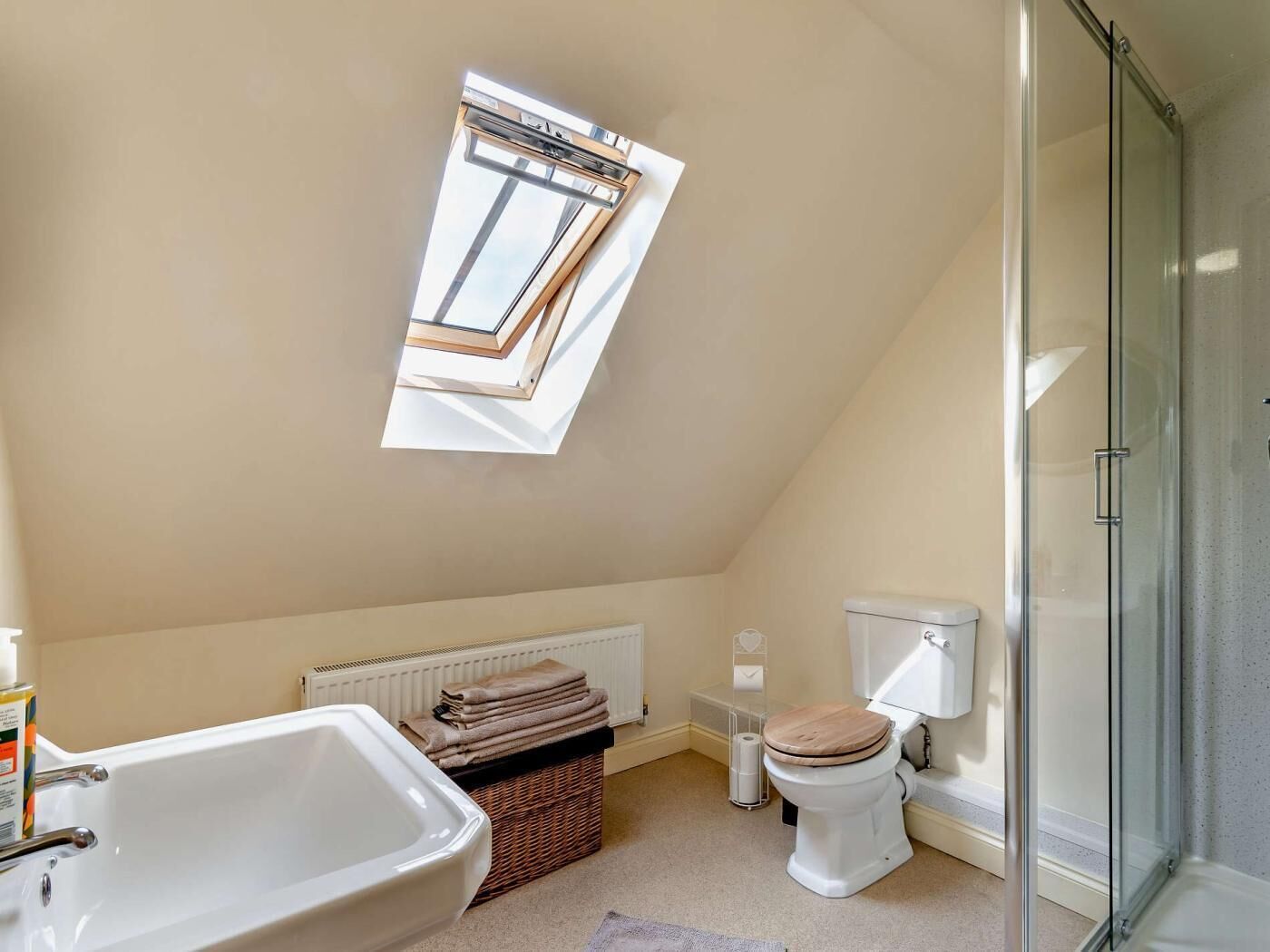 A bathroom with a skylight, a bathtub, a toilet, and a shower enclosure.