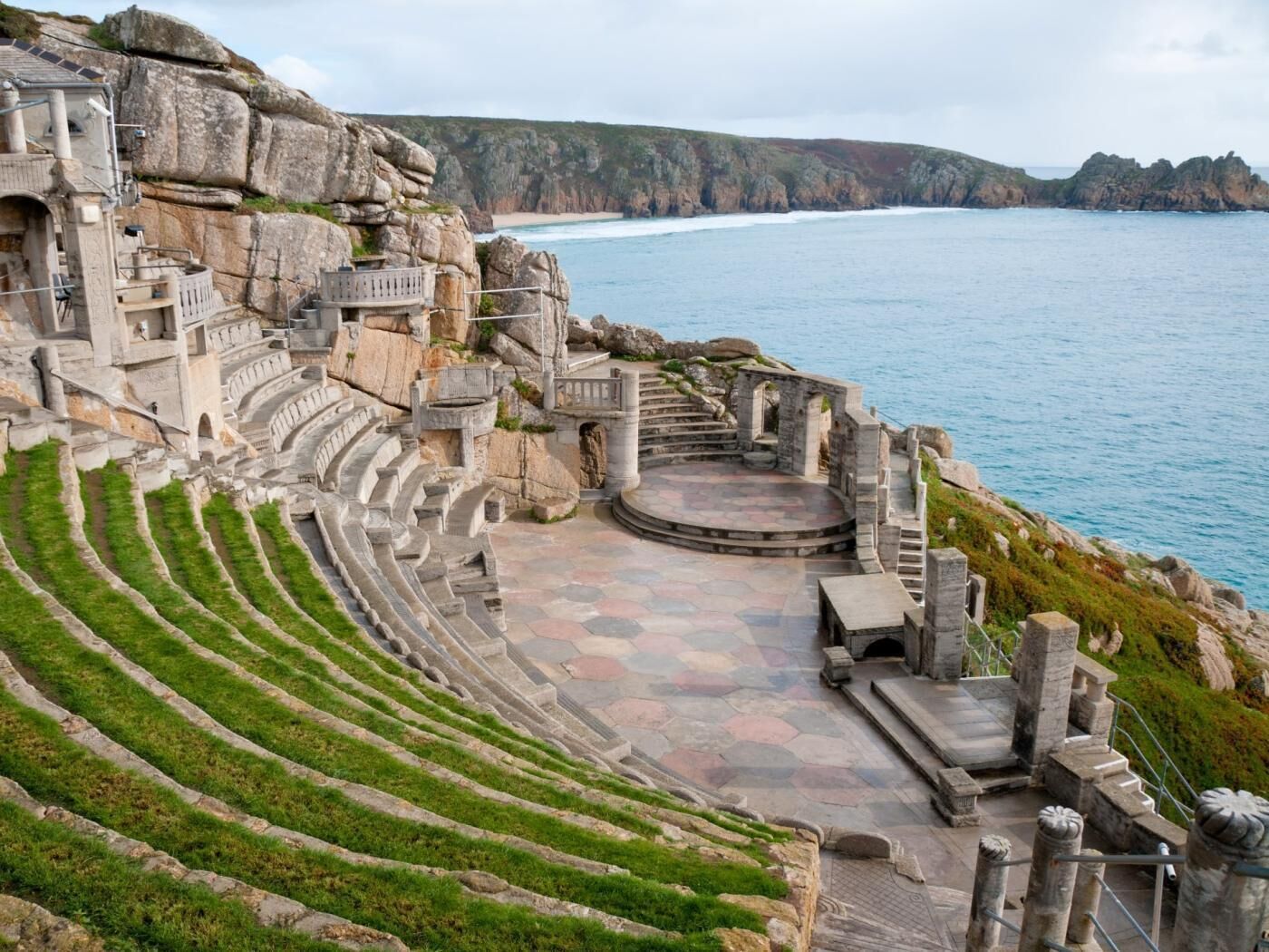 A stone amphitheater with tiered seating and a central stage, overlooking a coastal landscape.