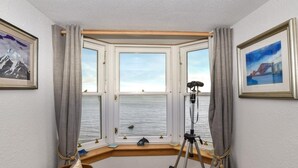 Een hoekkamer met erkerraam, uitzicht op water, een statief en twee ingelijste foto's.