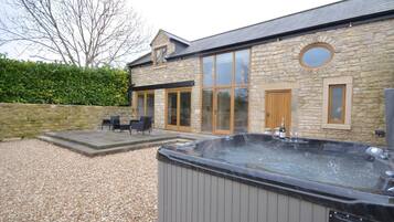 A stone building with a hot tub, outdoor seating, and a large window.