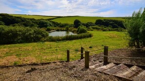 A rural landscape with a pond, grassy fields, and a wooden fence. - 4 Bed in Boscastle (oc-47035) (Forrabury and Minster)