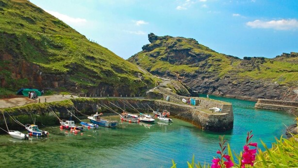 A coastal harbor with boats docked, a stone wall, and a hill in the background. - 4 Bed in Boscastle (oc-47035) (Forrabury and Minster)