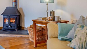 A cozy living room with a wood-burning stove, a table with a lamp, a coffee pot, and a basket. - 4 Bed in Boscastle (oc-47035) (Forrabury and Minster)