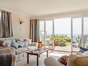 Een woonkamer met een bank, salontafel en uitzicht op zee door grote glazen deuren.