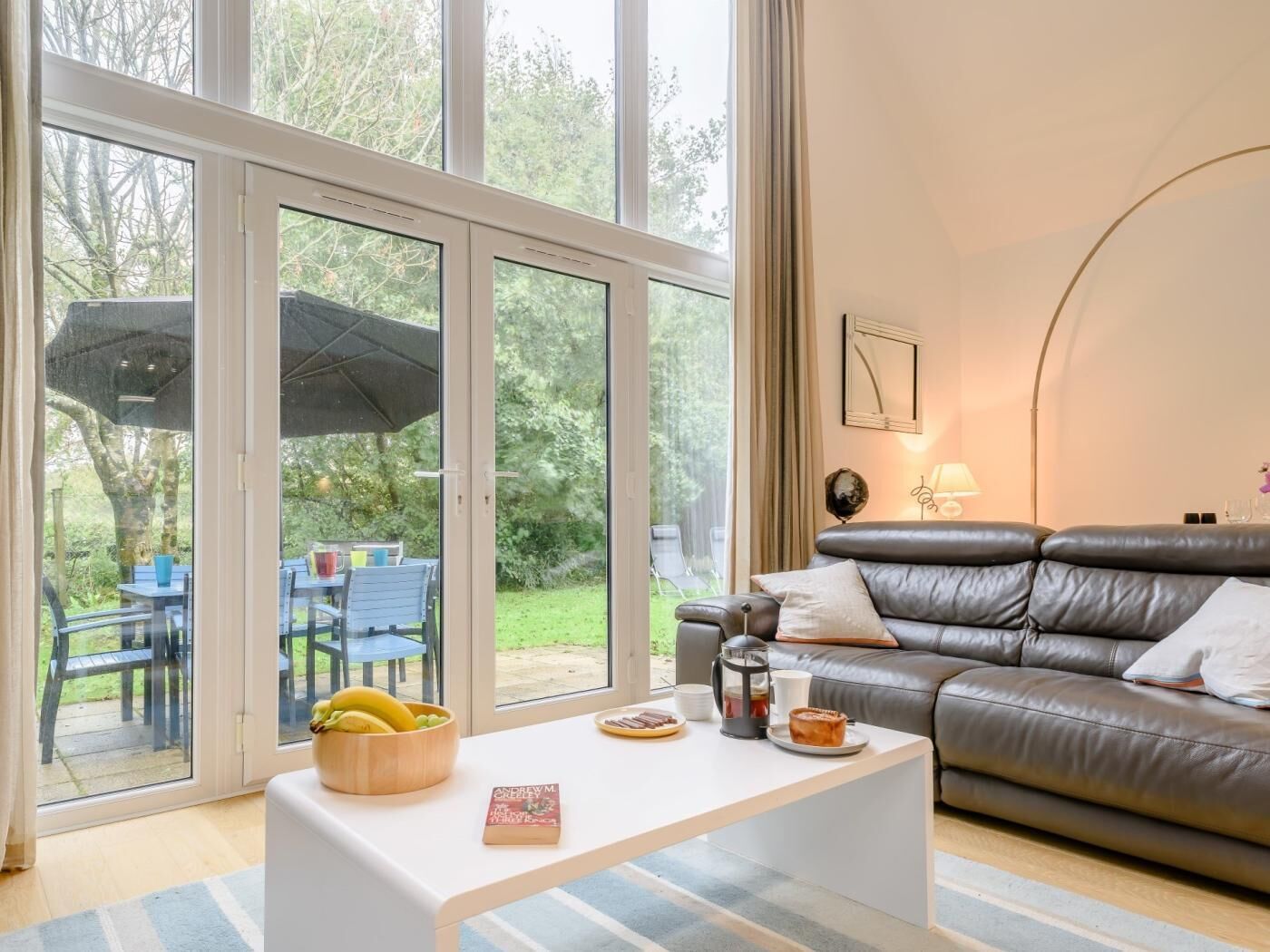 Ein modernes Wohnzimmer mit einem Ledersofa, einem weißen Couchtisch und einem Essbereich, der durch Glastüren sichtbar ist.