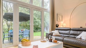 Un salon moderne avec un canapé en cuir, une table basse blanche et un coin repas visible à travers des portes vitrées.